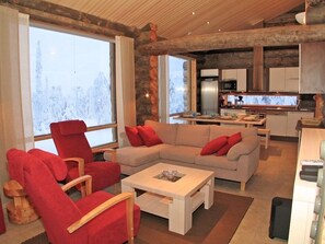 A modern living room with a large window, a sofa, a red armchair, and a coffee table. - Kelokoto Chalets (Kuusamo)
