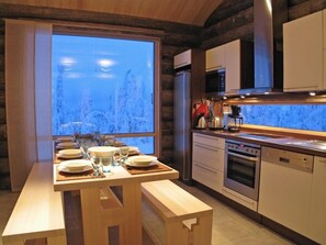 A modern kitchen with wooden cabinetry, a large window overlooking a snowy landscape, and a dining area with a wooden table set for four.