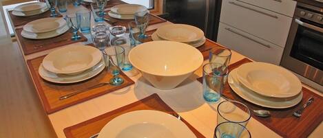 A dining table set for four with plates, glasses, and cutlery. A large bowl is centered on the table.