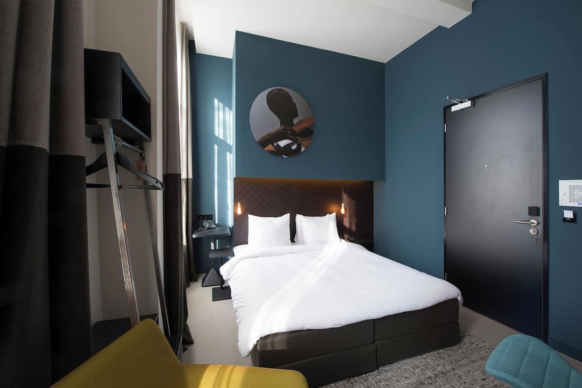Habitación de hotel con cama, mesita de noche, espejo, armario y puerta.