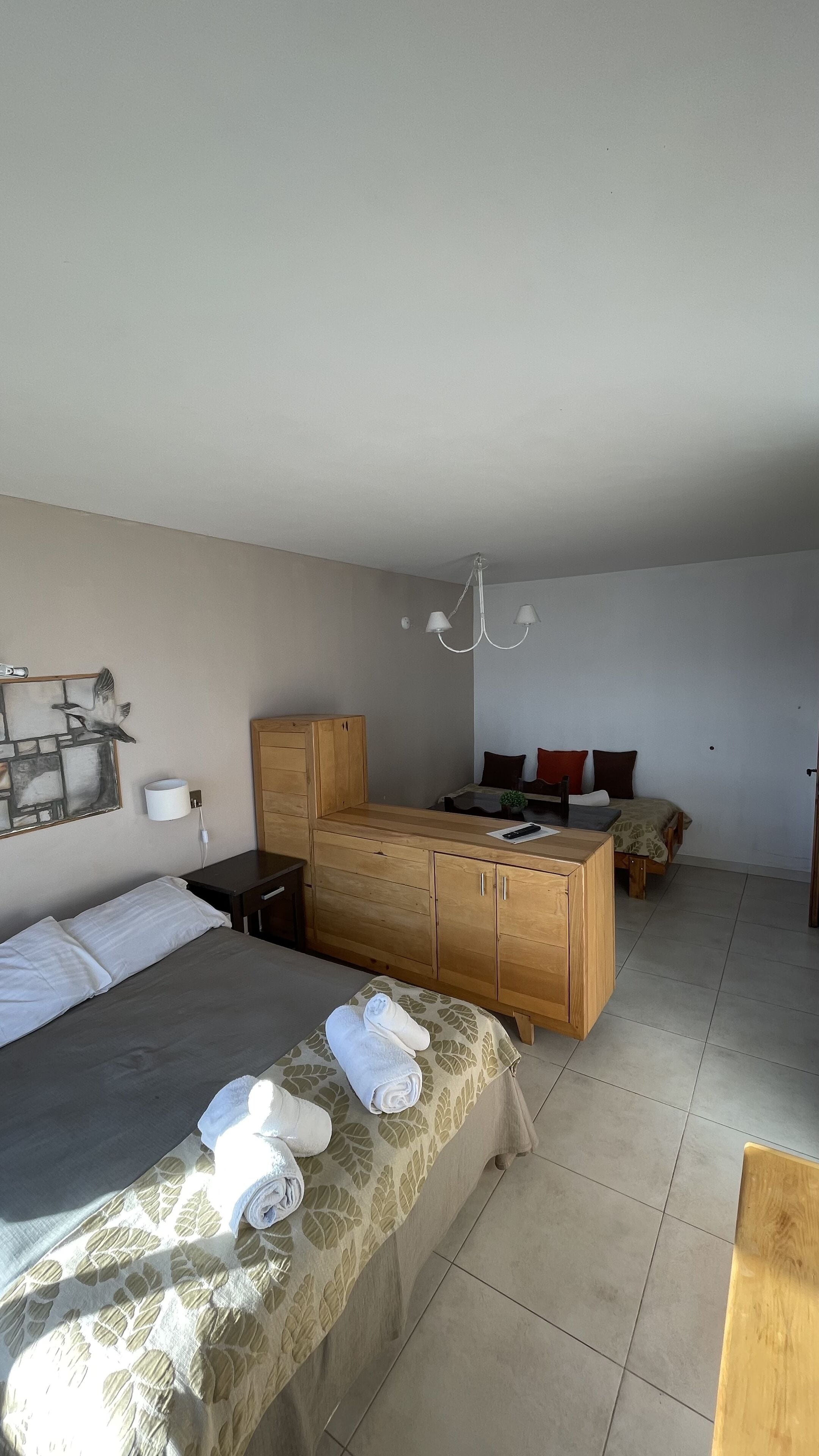 A bedroom with a bed, a wooden cabinet, a small table, and a hanging light fixture.