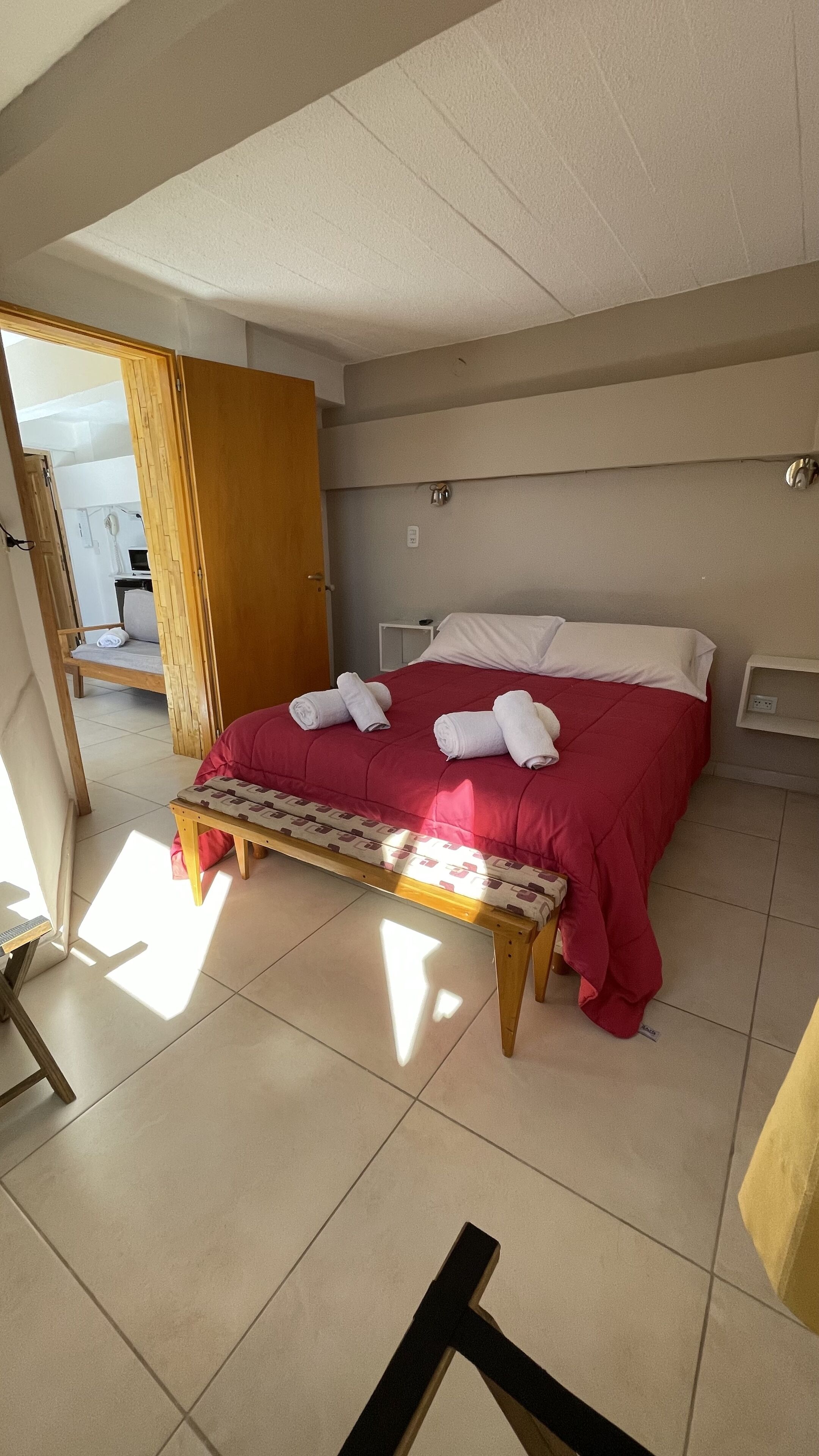 A hotel room with a bed, a bench, and a wooden door.
