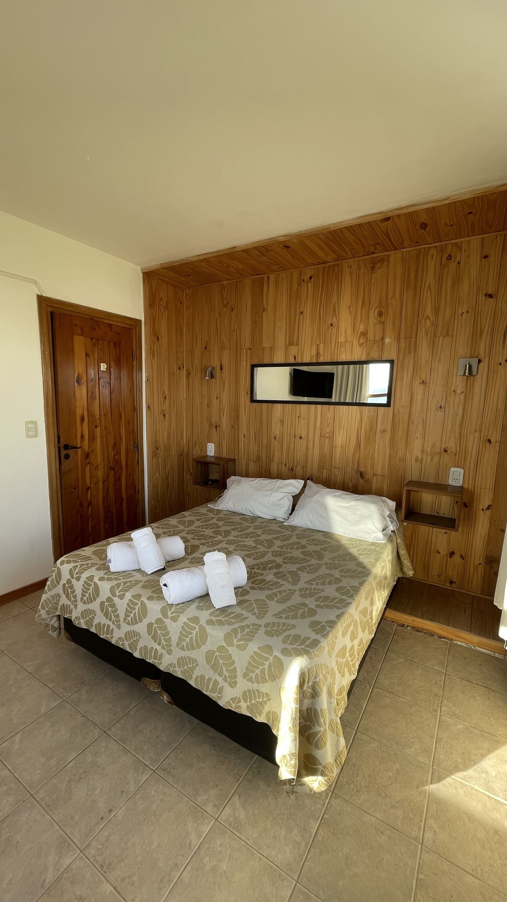 A bedroom with a bed, wooden panel walls, a mirror, and a tiled floor.