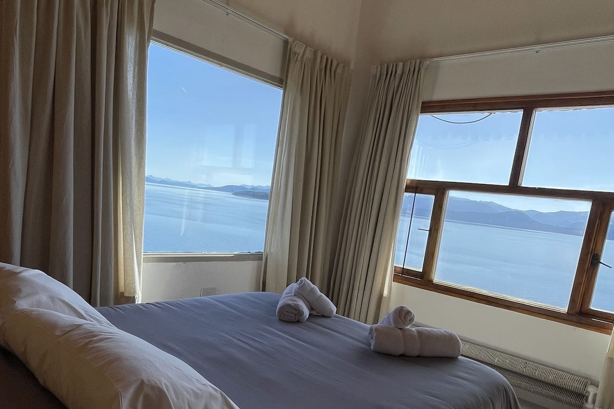 Ein Schlafzimmer mit einem großen Bett, zwei mit Vorhängen versehenen Fenstern und Meerblick.