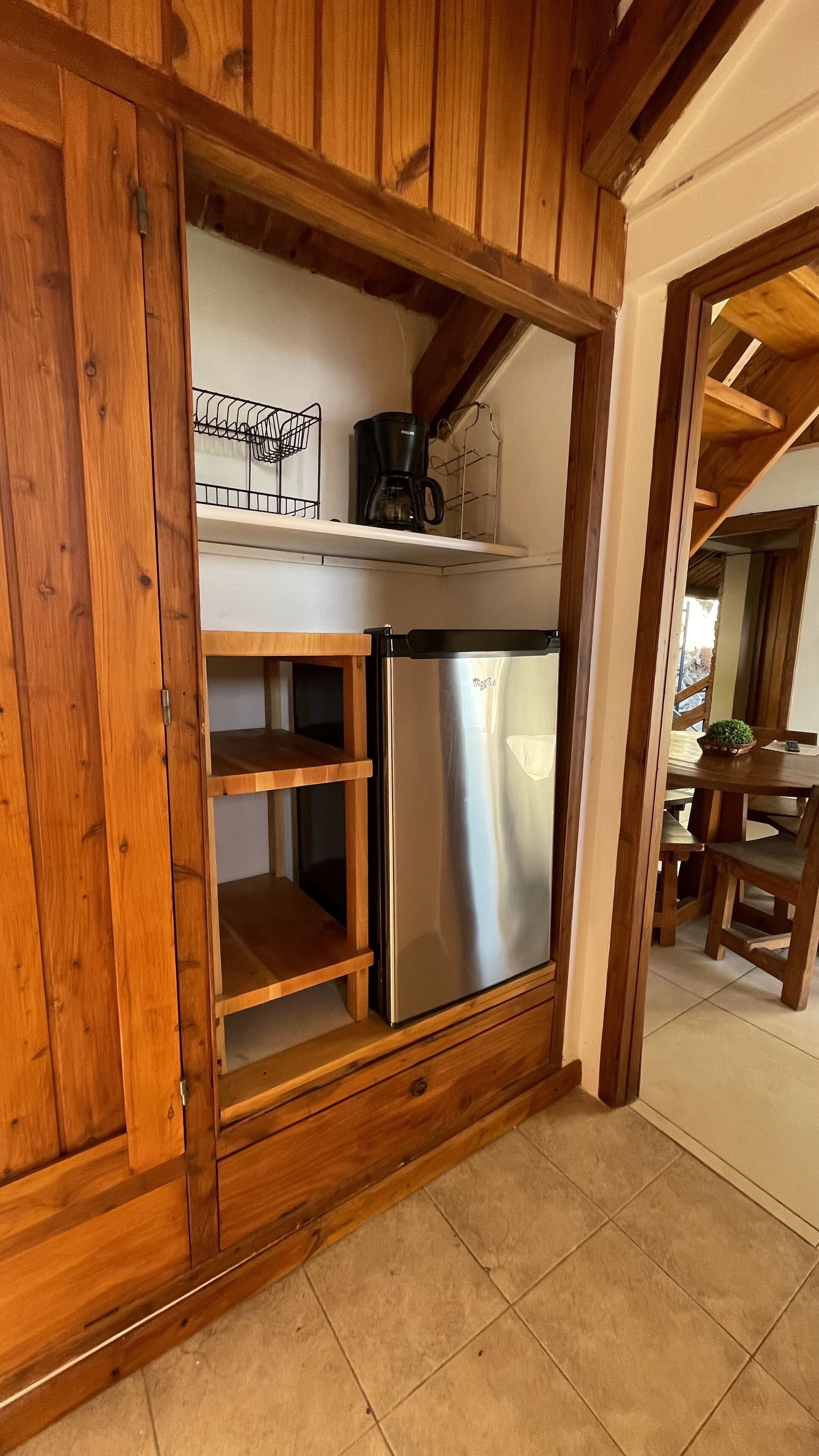 A kitchen with wooden cabinets, a stainless steel refrigerator, and a coffee maker on a shelf.