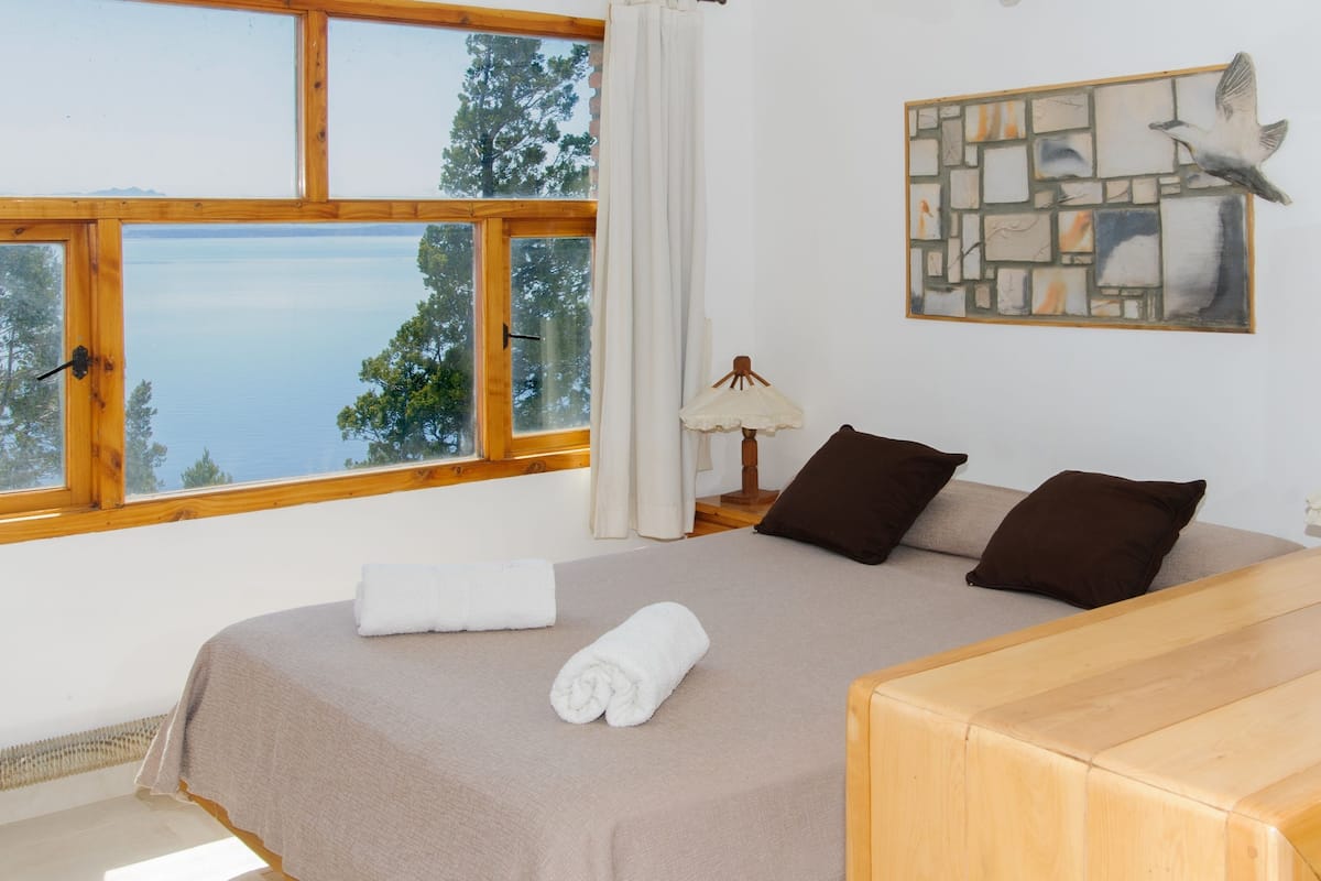 Ein Schlafzimmer mit einem großen Bett, einem Nachttisch aus Holz, einem Tisch und Meerblick durch ein Fenster.