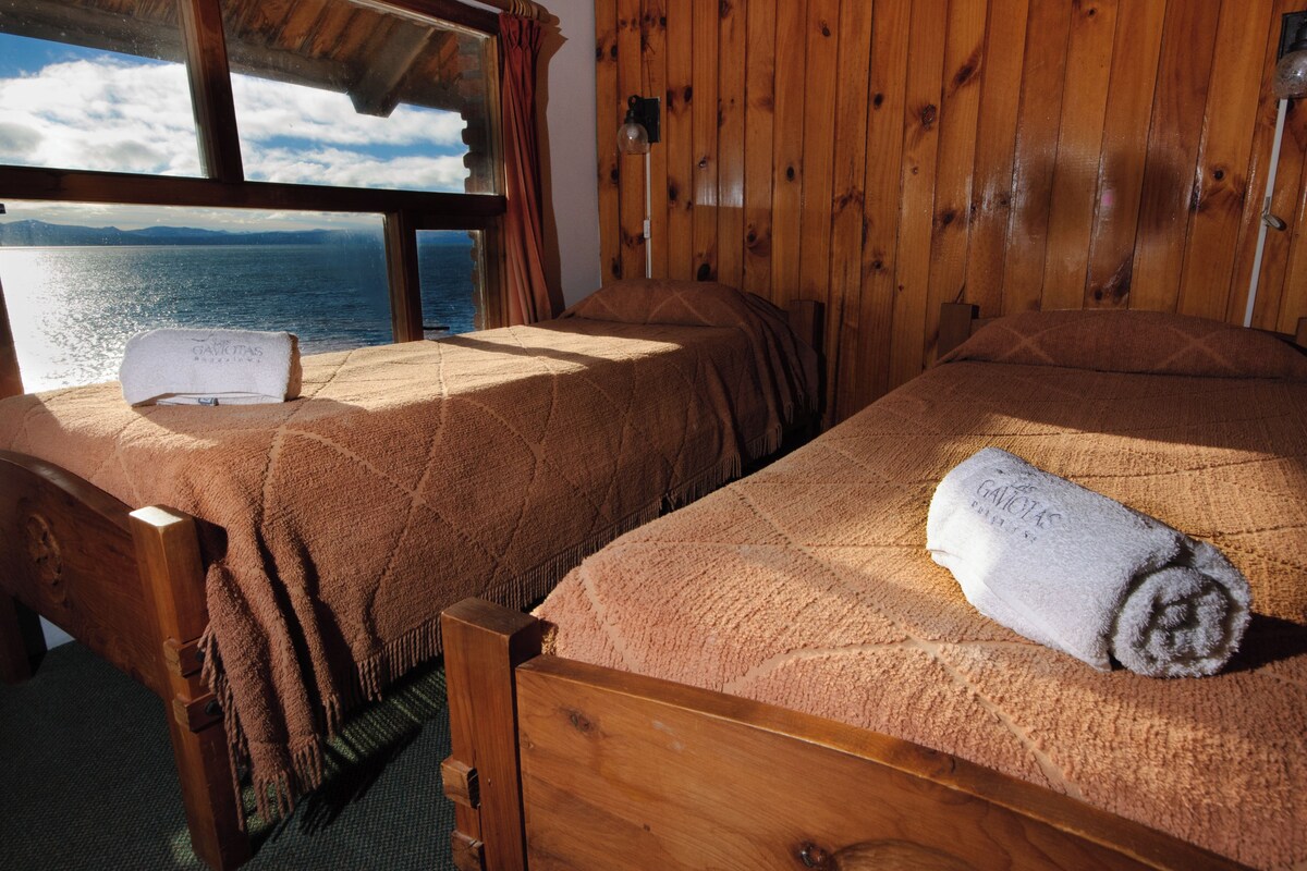 Une cabane en bois avec deux lits, chacun équipé d’une serviette et d’une couverture, et une vue sur la mer par la fenêtre.