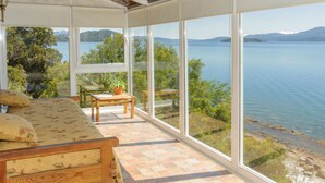 Une pièce baignée de lumière, avec une grande fenêtre donnant sur un lac, un canapé en bois et une petite table sur laquelle est posée une plante.