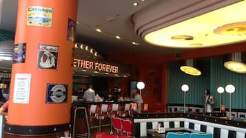 A restaurant interior with a neon sign reading "EITHER FOREVER," red and blue chairs, and a counter with a man in a white shirt.