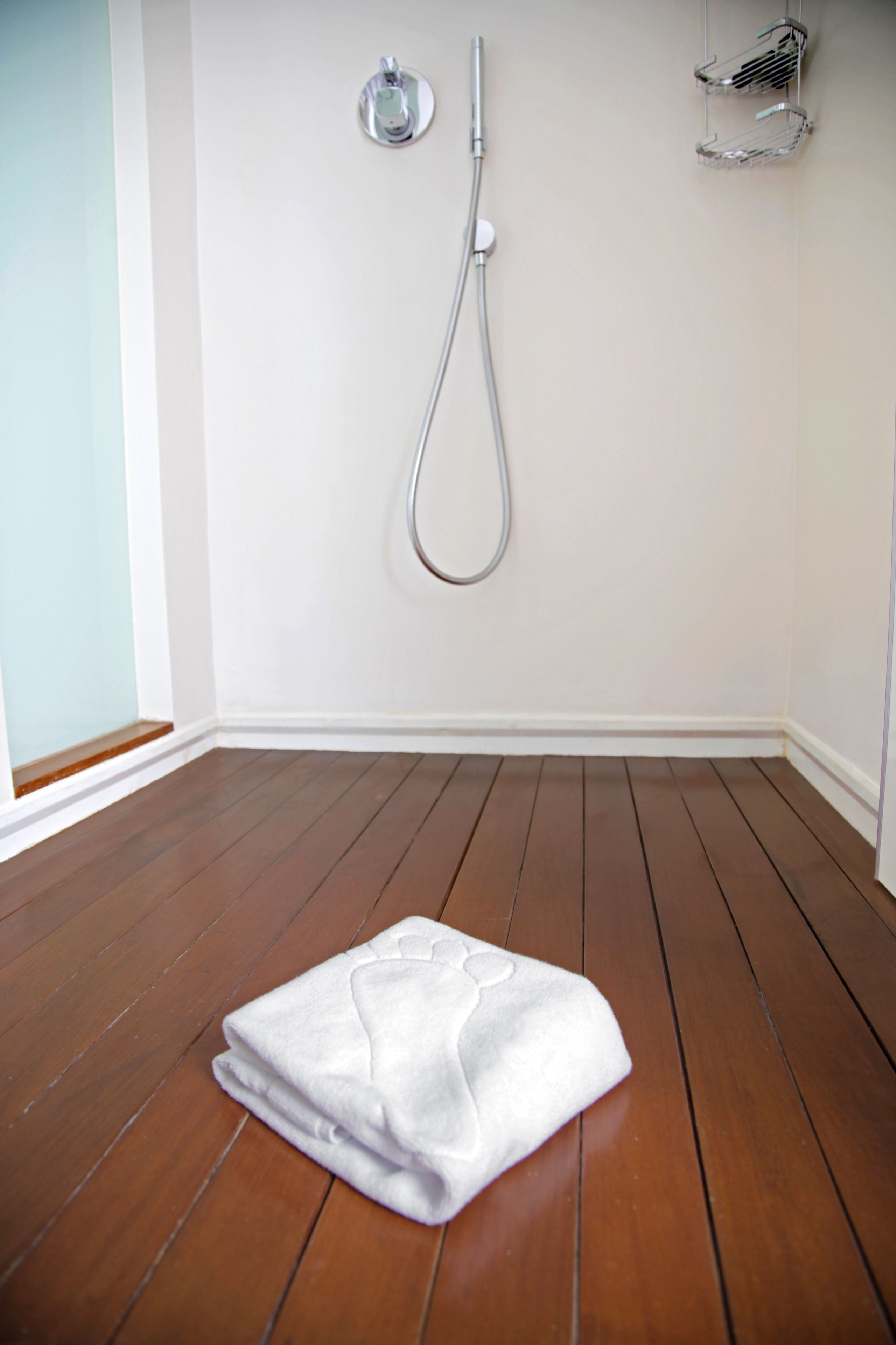Un baño con piso de madera, una toalla blanca, una ducha y un perchero de cromo.