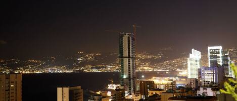 Una vista nocturna del paisaje urbano con edificios altos, incluyendo un rascacielos en construcción.