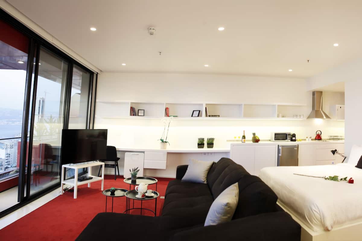 Una habitación de hotel moderna con una cama grande, un sofá, una pequeña mesa de comedor y una zona de cocina.