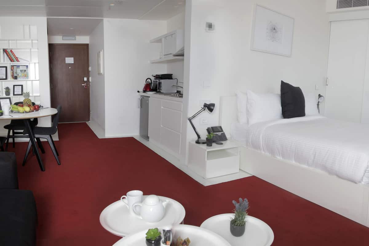 Una habitación de hotel moderna con cama, escritorio, kitchenette y zona de estar con alfombra roja.