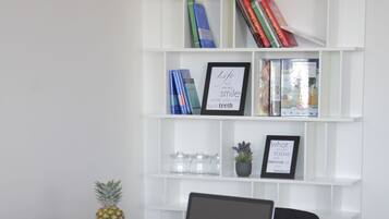 A workspace with a laptop on a white table, two black chairs, a fruit bowl, and a white bookshelf with books and decorative items.