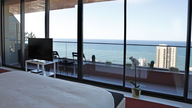 A modern hotel room with a large balcony, a bed, a TV, and a dining area with a view of the sea. - 1866 Court & Suites (Beirut)