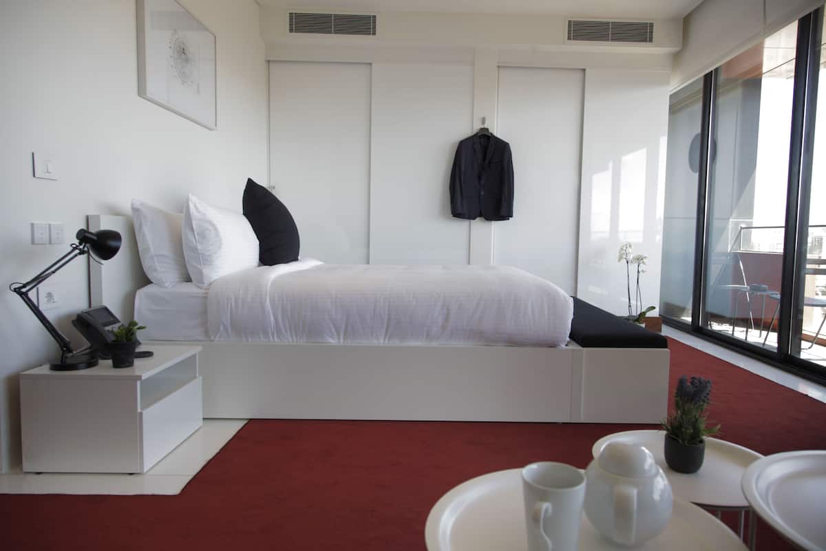 Un dormitorio moderno con cama, mesita de noche, lámpara y vistas al exterior a través de amplias ventanas.