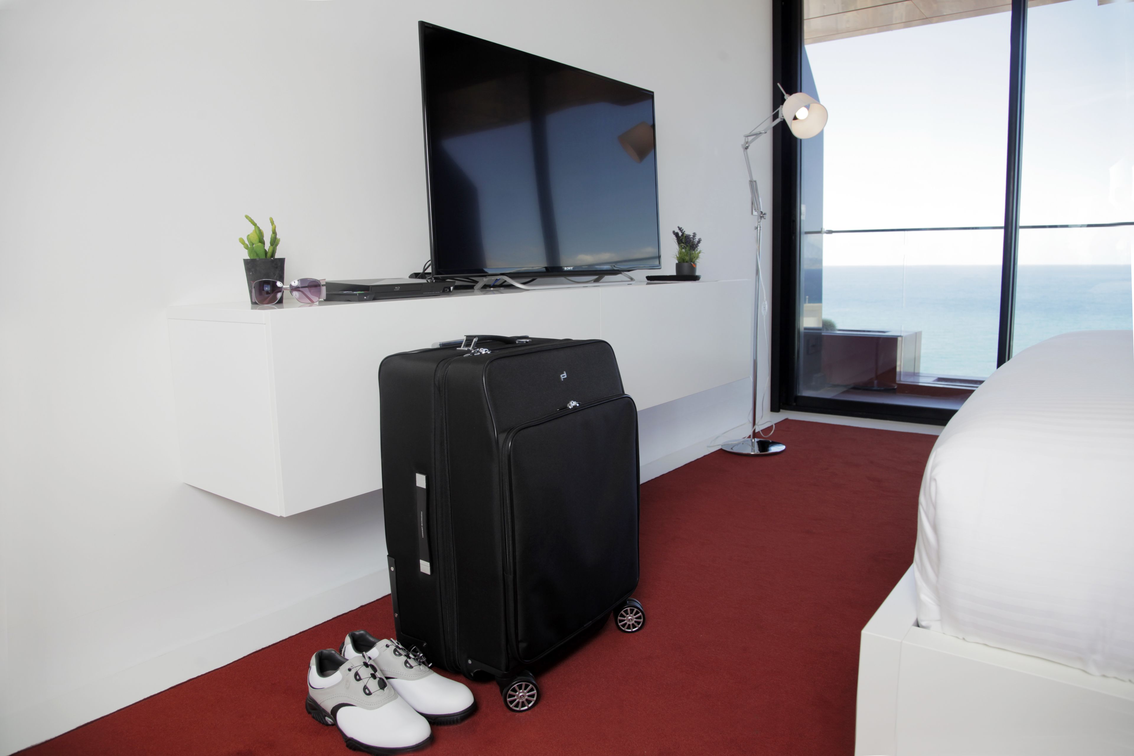 Habitació d'hotel amb un televisor gran, una maleta, un parell de sabates i un llit.