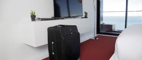 A hotel room with a large TV, a suitcase, a pair of shoes, and a bed.