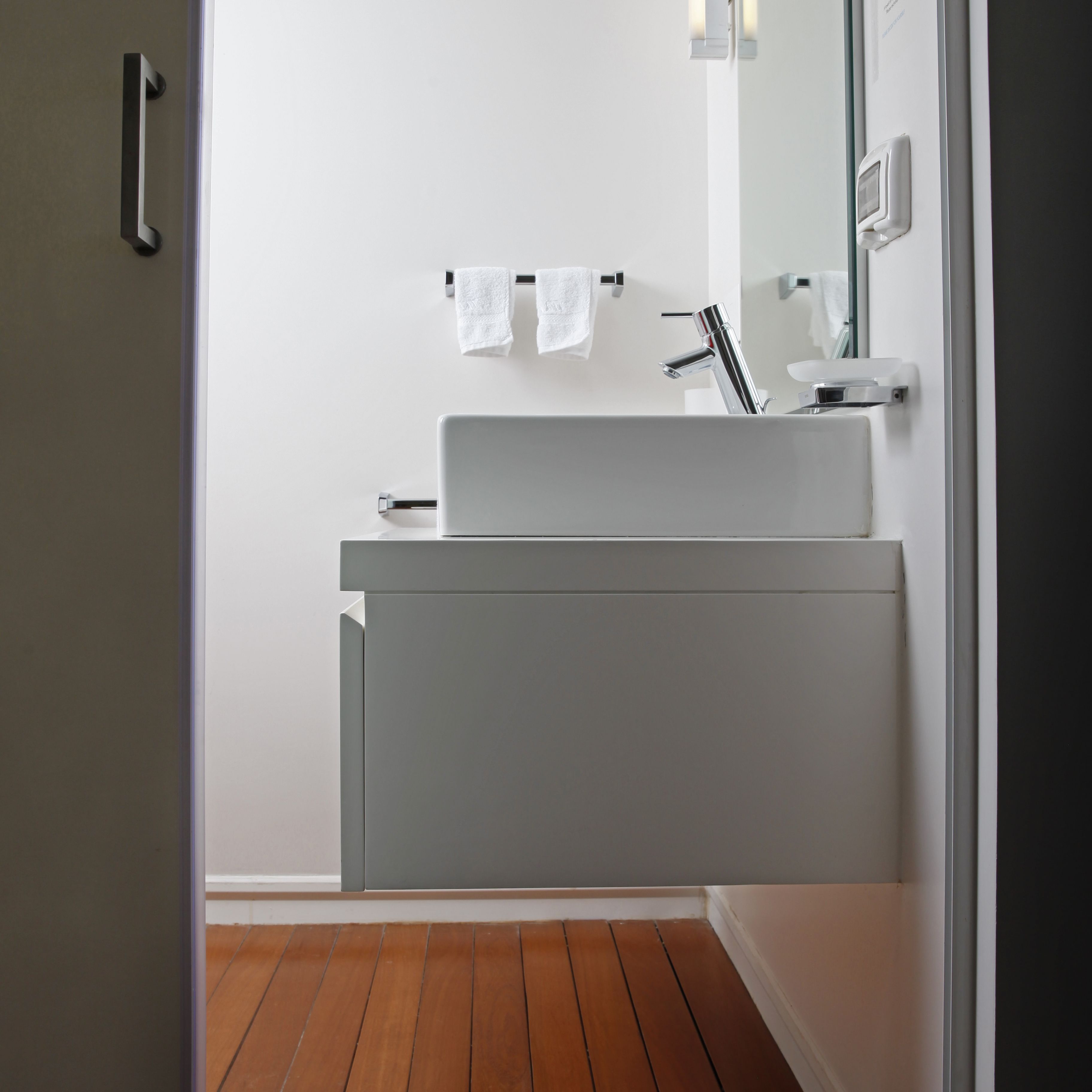 Un baño moderno con un lavamanos blanco, un espejo y un perchero para toallas.