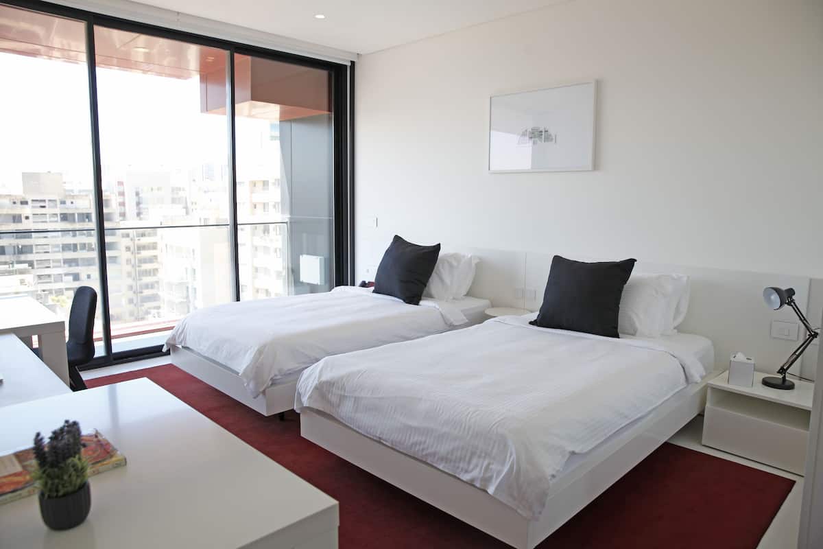 Una habitación de hotel moderna con dos camas, un escritorio y un amplio ventanal con vistas a la ciudad.