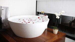 A modern bathroom with a large white bathtub filled with rose petals, a small potted orchid, and two glasses of champagne on a white side table. - 1866 Court & Suites (Beirut)