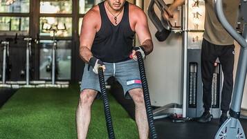 Une salle de sport dotée d’un revêtement de sol synthétique, d’appareils d’exercice et où une personne s’entraîne avec des cordes de combat.