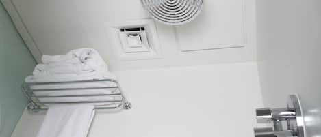 A corner of a bathroom with a shower, a towel rack, a fan, and a small shelf.