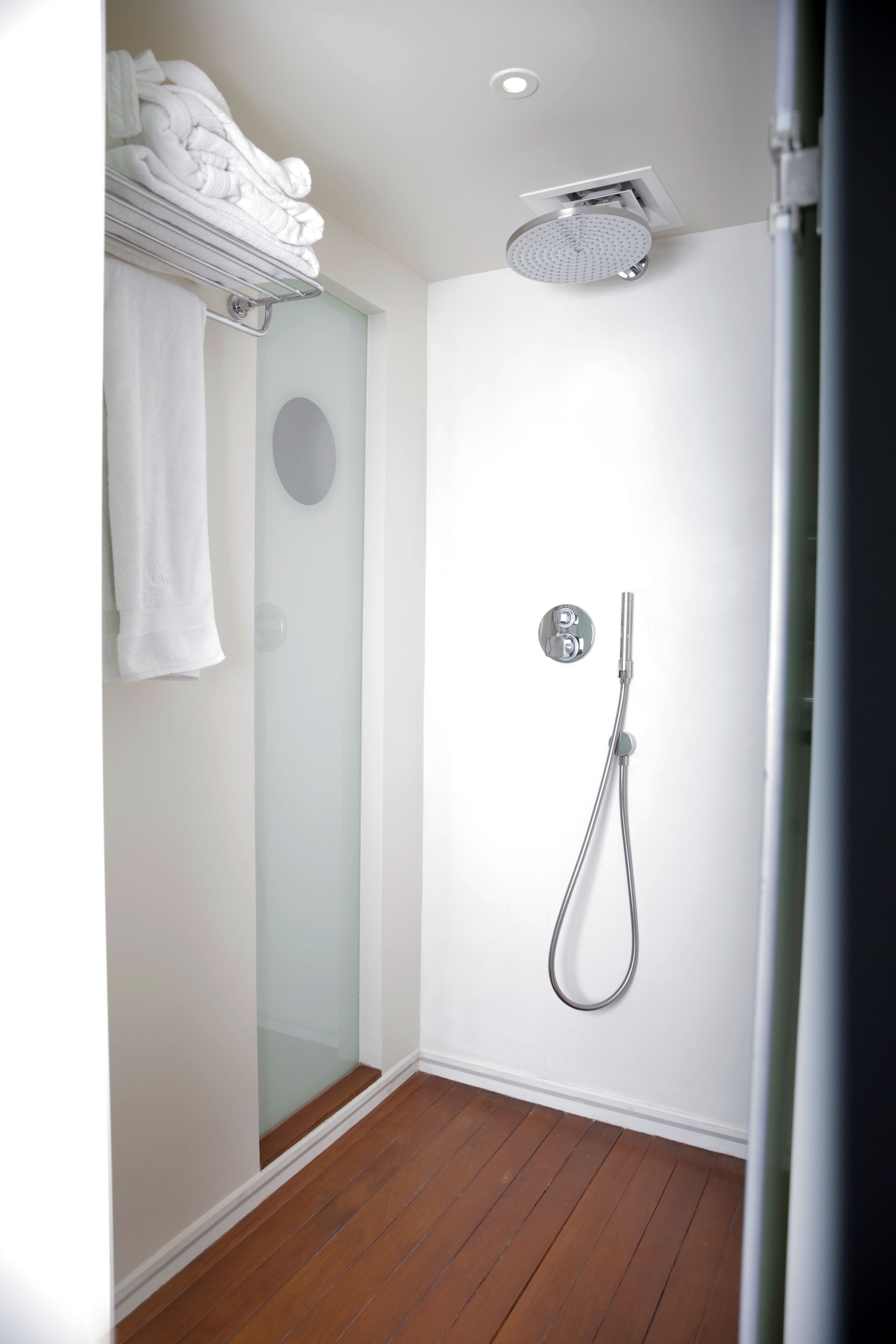 A modern bathroom with a glass shower enclosure, a towel rack with folded towels, a showerhead, and a toilet.