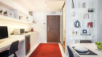 Una cocina moderna con armarios blancos, microondas, cafetera y fregadero. Hay una zona de comedor con una mesa, sillas y un cuenco de fruta.