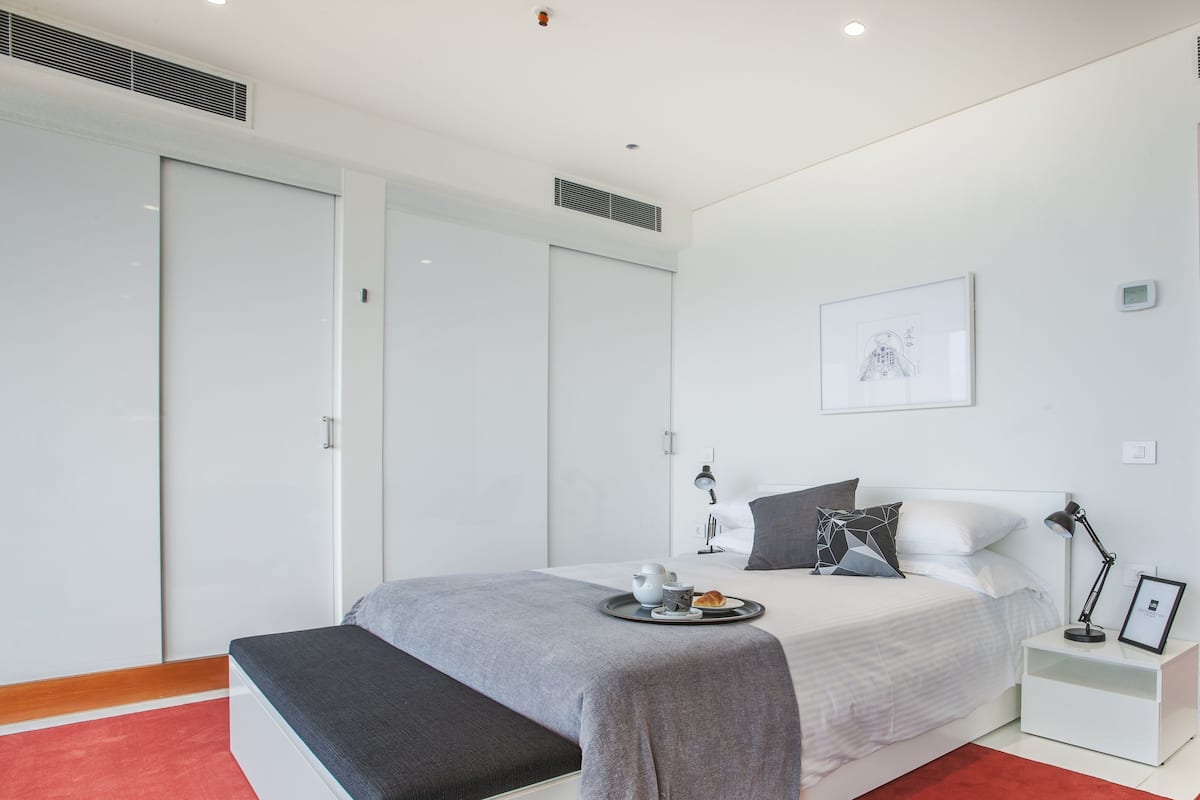 Un dormitorio moderno con una cama grande, mesitas de noche, un banco y una alfombra roja.