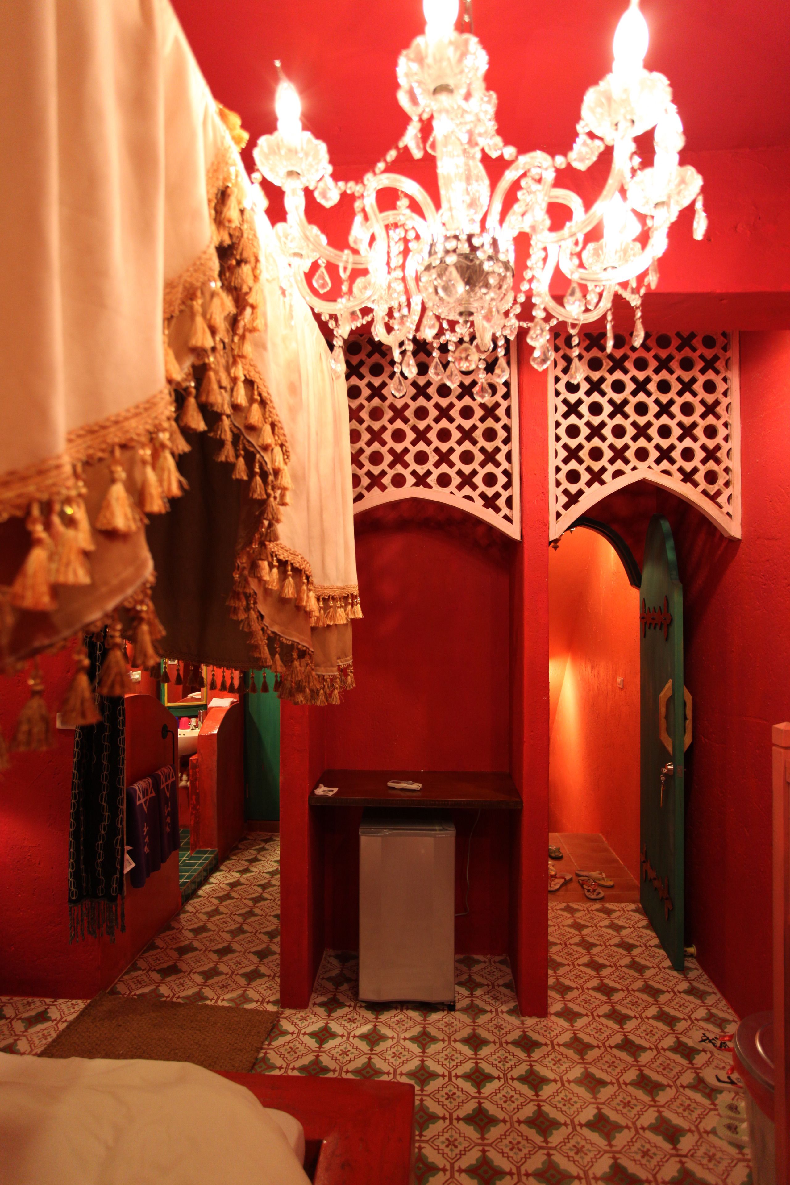 A room with a patterned floor, a chandelier, a bed, and a small table.