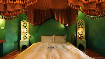 Una cama con cabecera verde, dos mesitas de noche con lámparas y una cortina decorativa.