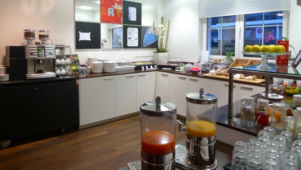 A modern kitchen with a coffee machine, a fruit display, and a bulletin board. - Businesshotel LUX (Emmen)