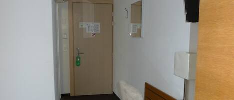 A hotel room with a wooden desk, a chair, a television mounted on the wall, and a door with a sign.