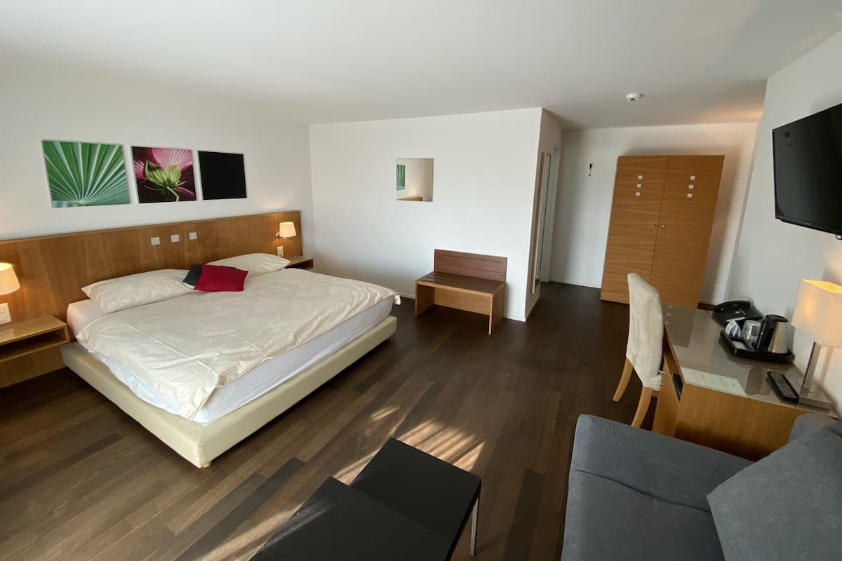 A hotel room with a large bed, bedside tables, a desk, a chair, a wardrobe, and a TV.