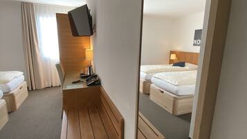 A hotel room with a wooden desk, a bed, a mirror, and a TV mounted on the wall.