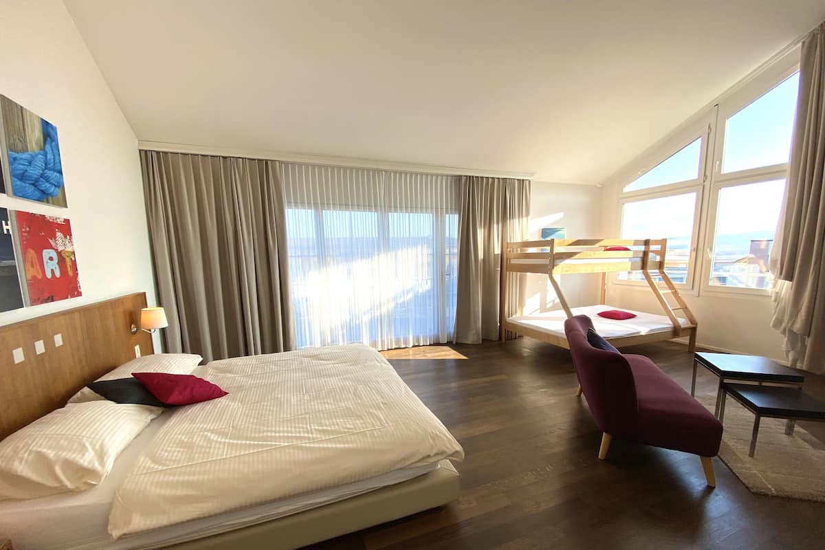 A hotel room with a large bed, a desk, a chair, and a bunk bed.