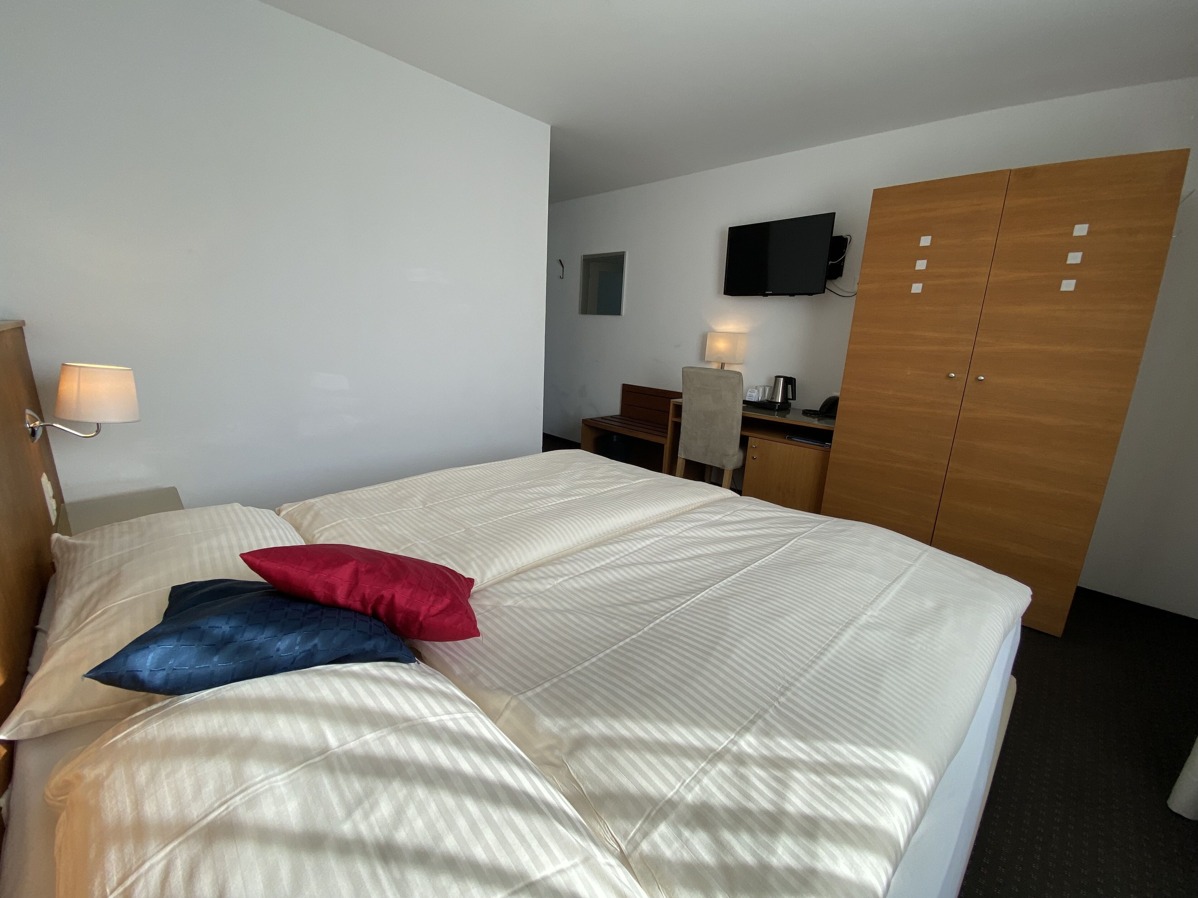 A hotel room with a bed, a desk, a TV, and a wardrobe.