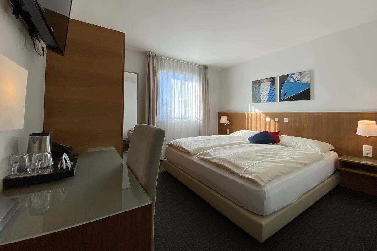 A hotel room with a bed, a desk, a chair, a TV, and a window with curtains.