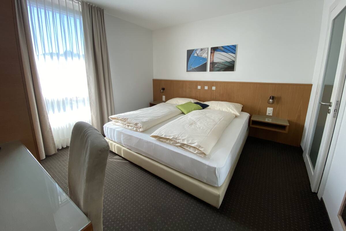 A hotel room with a bed, a desk, and a chair. There are two wall-mounted lamps and a small nightstand.