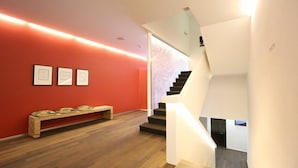 A modern interior with a wooden bench, a staircase, and framed artwork on the wall. - Businesshotel LUX (Emmen)