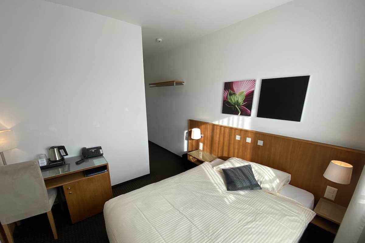 A hotel room with a bed, a desk with a coffee maker, a phone, and a lamp.