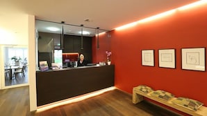 A reception area with a dark reception desk, a bench with cushions, and framed artwork on the wall. - Businesshotel LUX (Emmen)
