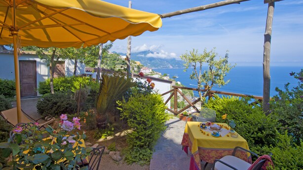 Eine Terrasse mit einem gelben Sonnenschirm, einem Esstisch und Blick auf das Meer.