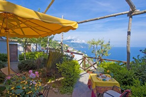 Une terrasse avec un parasol jaune, une table dressée pour le repas et une vue sur la mer.