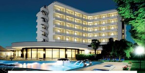 Ein mehrstöckiges Hotel mit Poolbereich, Außenbereich zum Sitzen und einer gut beleuchteten Fassade.