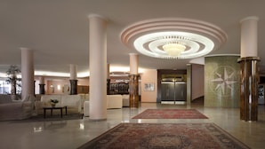 A spacious lobby with a central chandelier, large columns, and a patterned rug. - Hotel Commodore Terme (Montegrotto Terme)