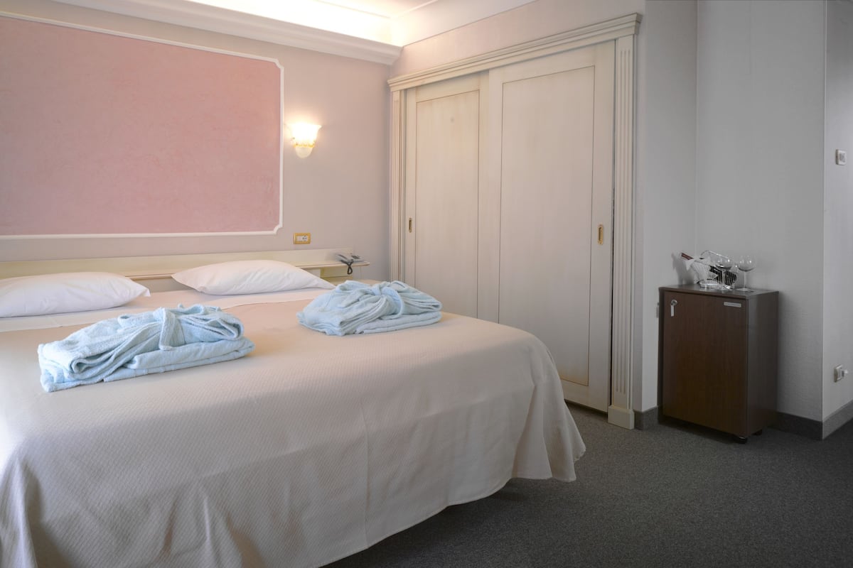 A hotel room with a bed, two bedside tables, a wardrobe, and a small cabinet.