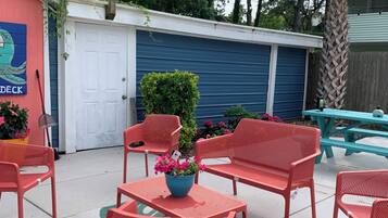 Un'area patio con sedie e tavoli in metallo rosso, una porta blu e una pianta verde come elemento decorativo.