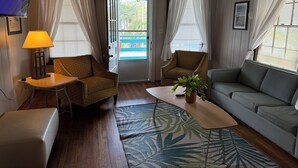 Una habitación acogedora con techo de madera, televisor, lámpara, sofá, silla, mesa de centro y una puerta que da al exterior.